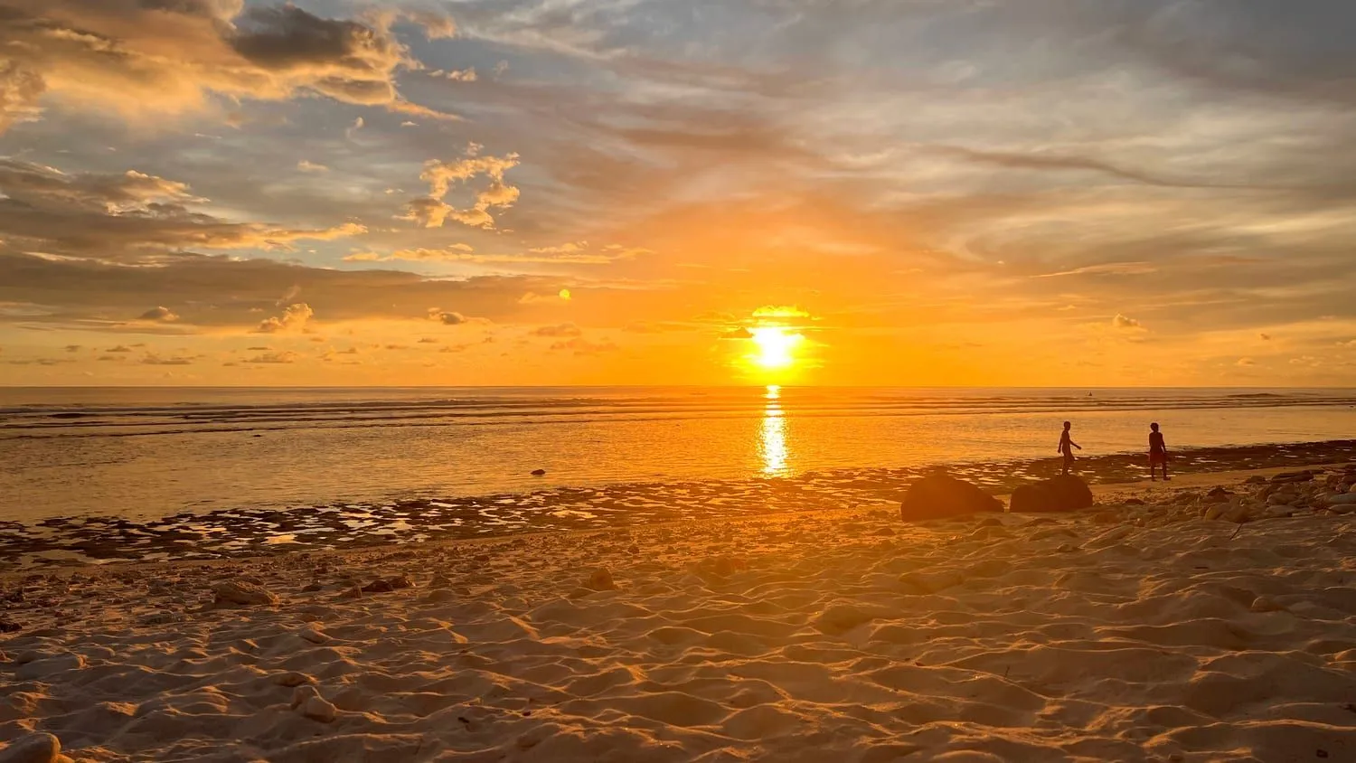 Sunset over the reef flat from the ocean side, with two people walking at the water line.